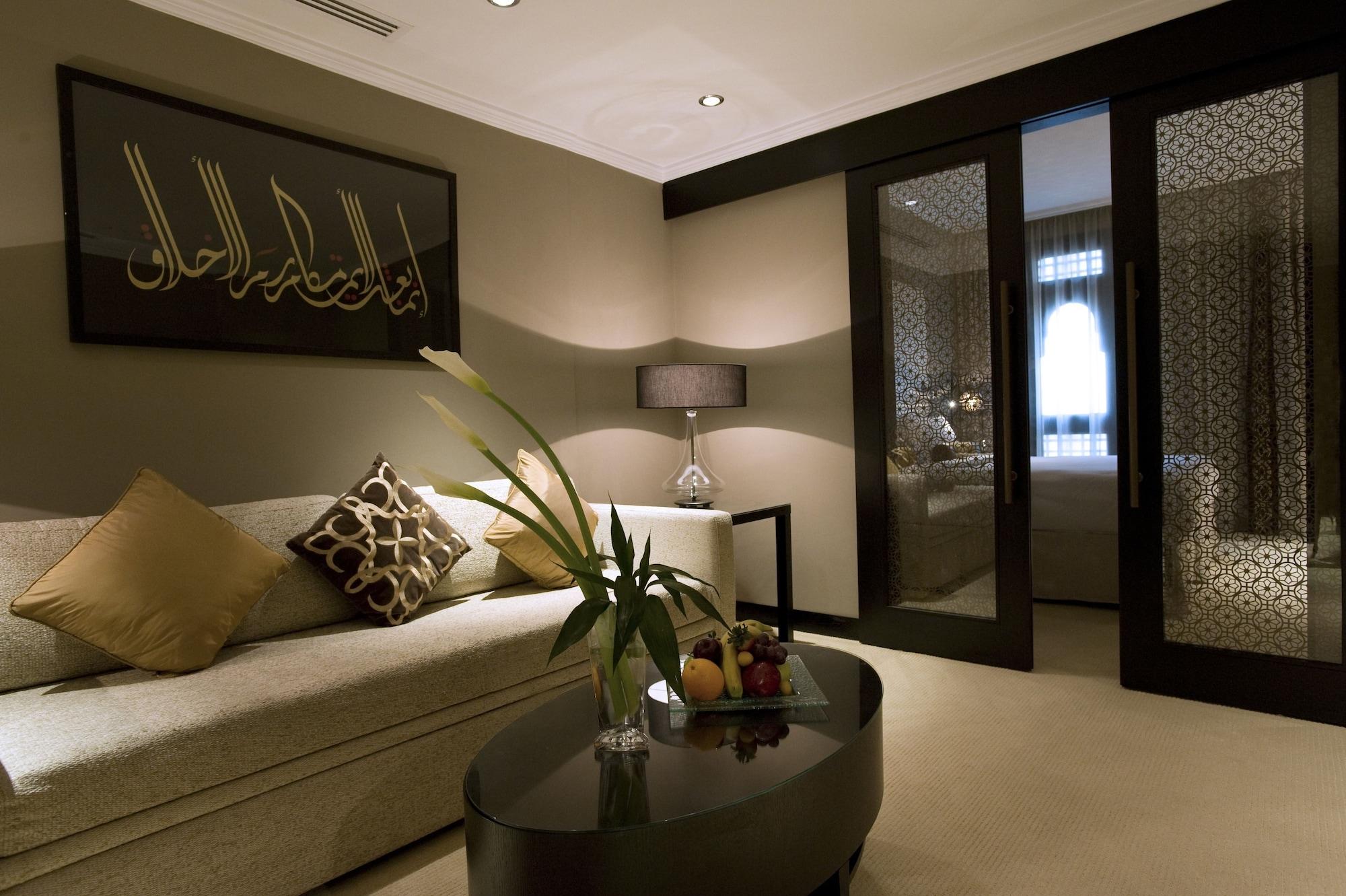 Sofitel Shahd Al Madinah Hotel Medina Exterior photo The photo shows a modern and elegantly designed lounge area. There is a light-colored sofa adorned with decorative cushions. A sleek, dark coffee table sits in front of the sofa, topped with a small vase containing flowers and a fruit arrangement. To