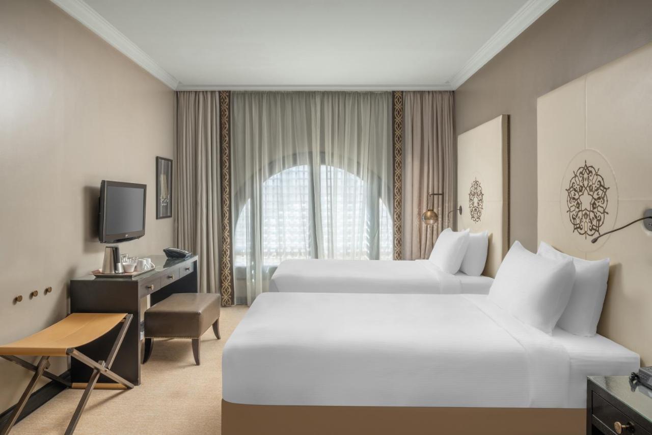 Sofitel Shahd Al Madinah Hotel Medina Exterior photo The photo shows a hotel room with a modern and minimalist design. There are two neatly made twin beds with white linens. A small table and an armchair are positioned near the window, which is draped with sheer curtains allowing natural light to enter