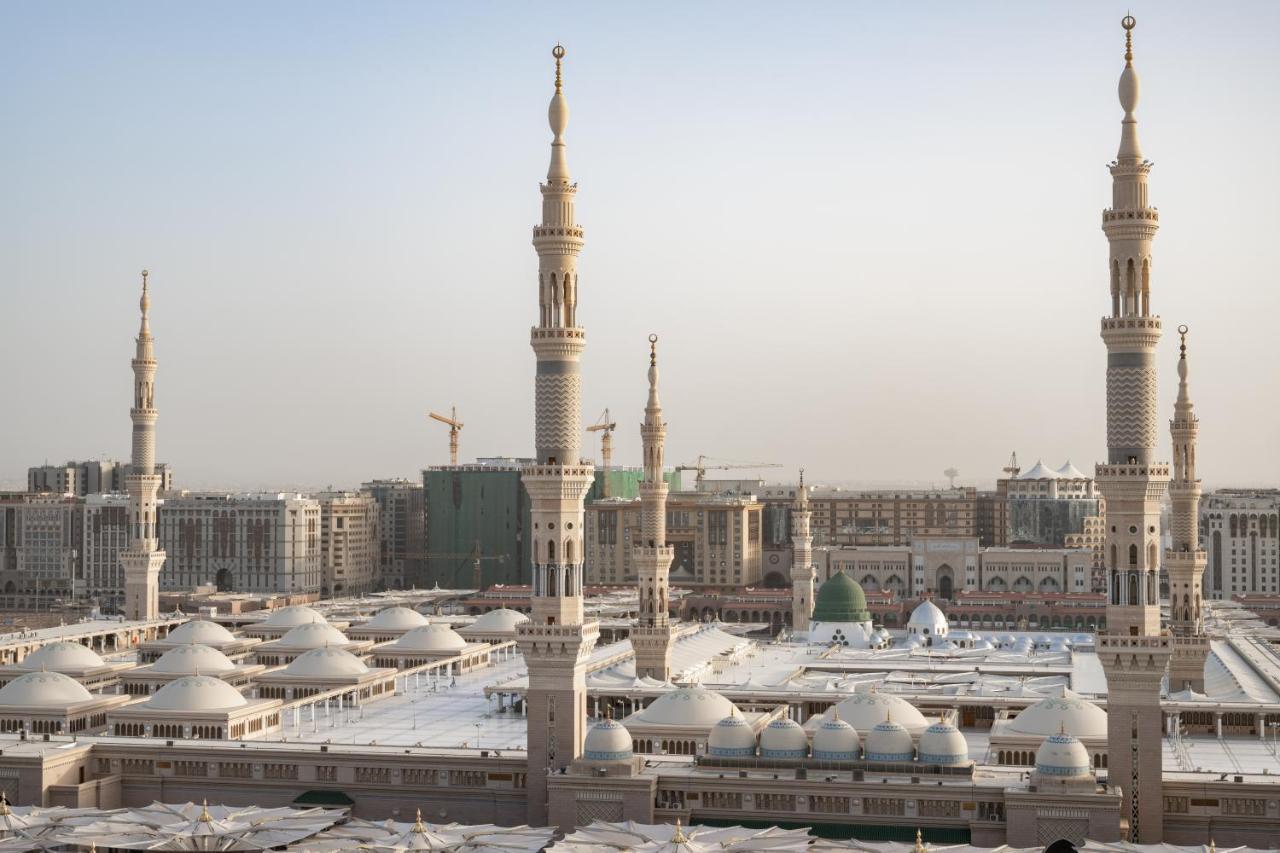 Sofitel Shahd Al Madinah Hotel Medina Exterior photo The photo depicts a view of an Islamic mosque complex with several prominent minarets. The architectural style features a blend of intricate designs and large, domed roofs. The scene appears to be set in a modern urban environment, with construction 