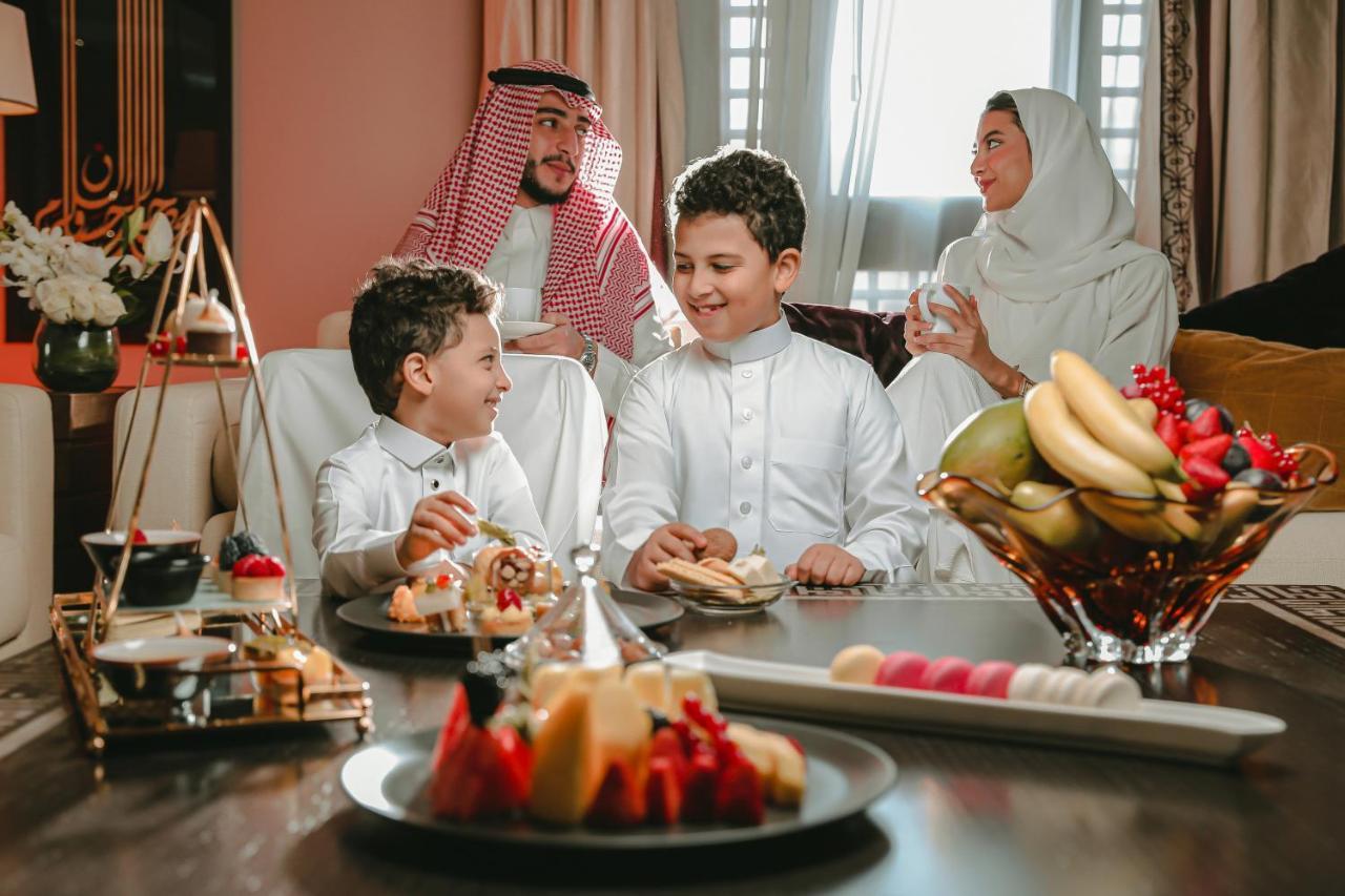 Sofitel Shahd Al Madinah Hotel Medina Exterior photo The photo shows a warm family moment featuring two young boys, dressed in traditional attire, engaged in a joyful conversation. They are seated around a table adorned with various dishes, including an array of fruits and pastries. In the background, 