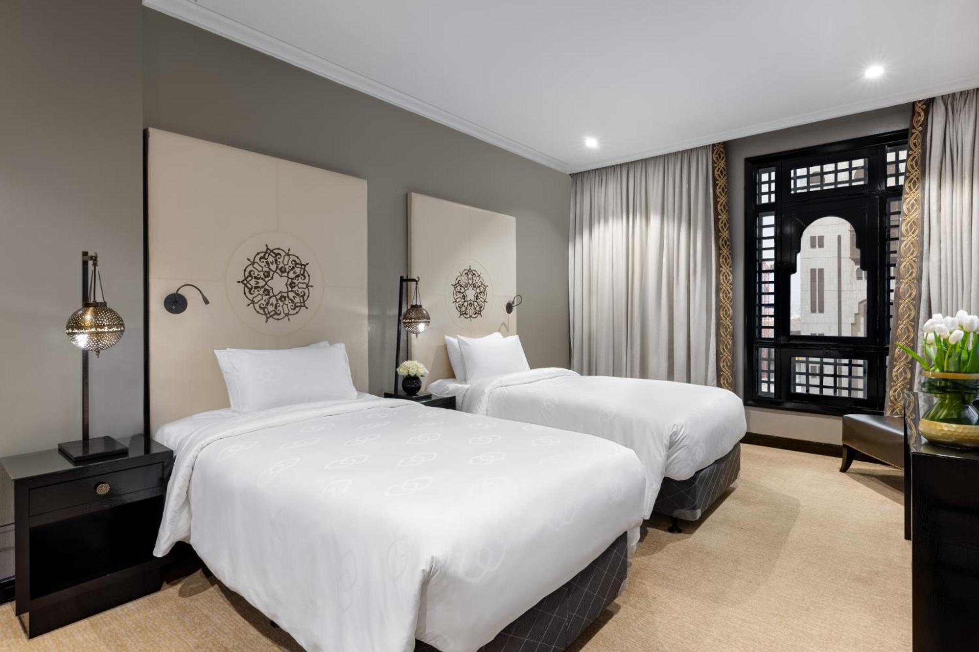 Sofitel Shahd Al Madinah Hotel Medina Exterior photo The photo shows a modern hotel room featuring two twin beds with white linens. Each bed is flanked by bedside tables with stylish lamps. The walls are painted in a neutral tone, and there are decorative panels behind the beds, adding a touch of elega