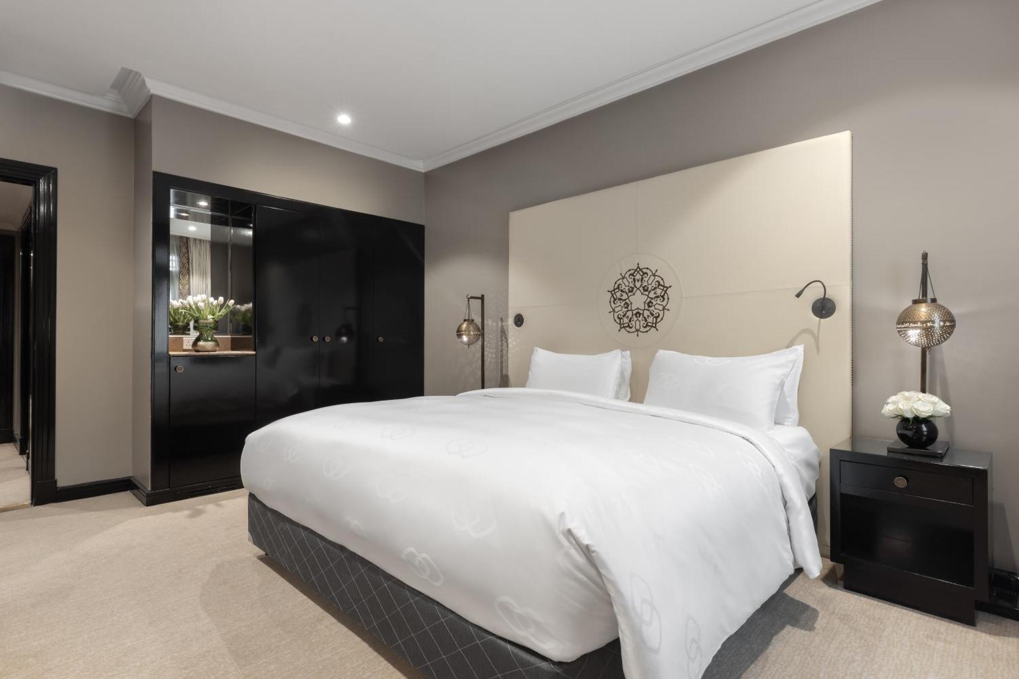Sofitel Shahd Al Madinah Hotel Medina Exterior photo The photo displays a modern and stylish bedroom. It features a large bed with white linens and two pillows, placed against a light-colored wall with an elegant headboard design. On each side of the bed, there are bedside tables with lamps that add a 