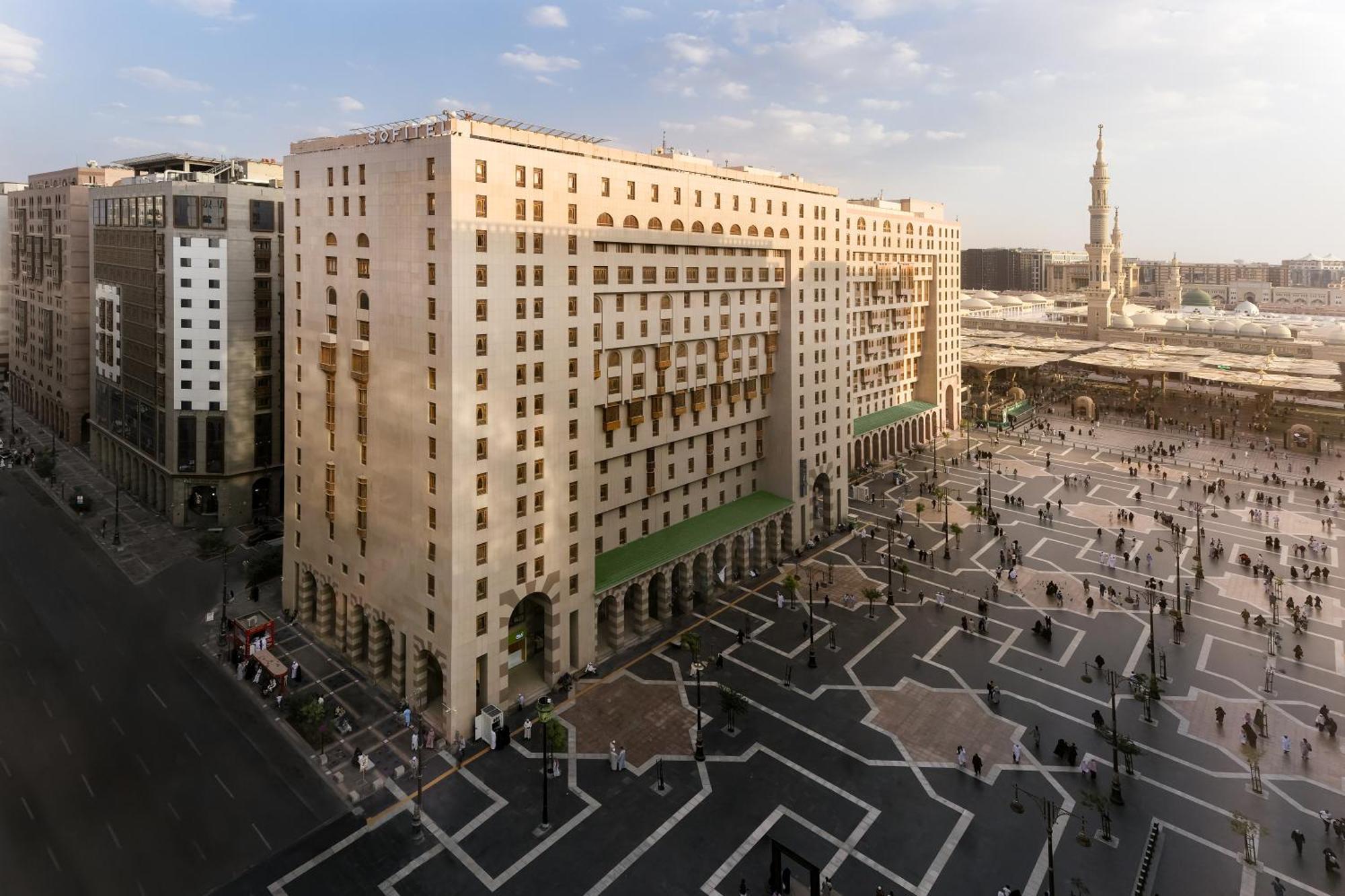 Sofitel Shahd Al Madinah Hotel Medina Exterior photo The photo shows a large, multi-story building with a distinct architectural design, located near a spacious outdoor plaza. The building features a combination of columns and large windows, giving it a formal appearance. In front of the building, ther