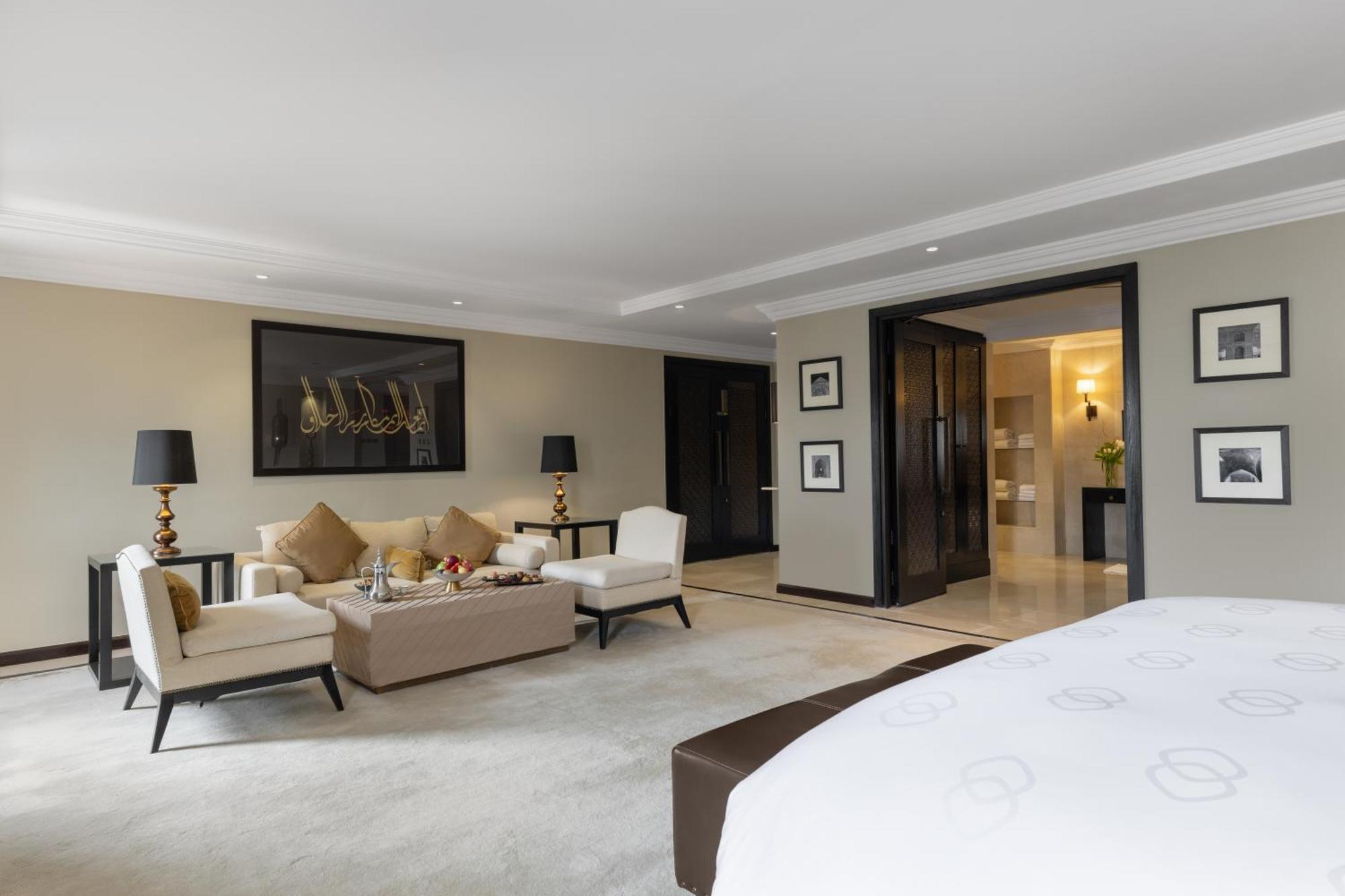 Sofitel Shahd Al Madinah Hotel Medina Exterior photo The photo depicts a spacious and elegantly designed hotel suite. In the foreground, there is a large bed with a dark headboard. To the right of the bed, there is a plush carpeted area. 

In the living area, there are two light-colored armchairs and a