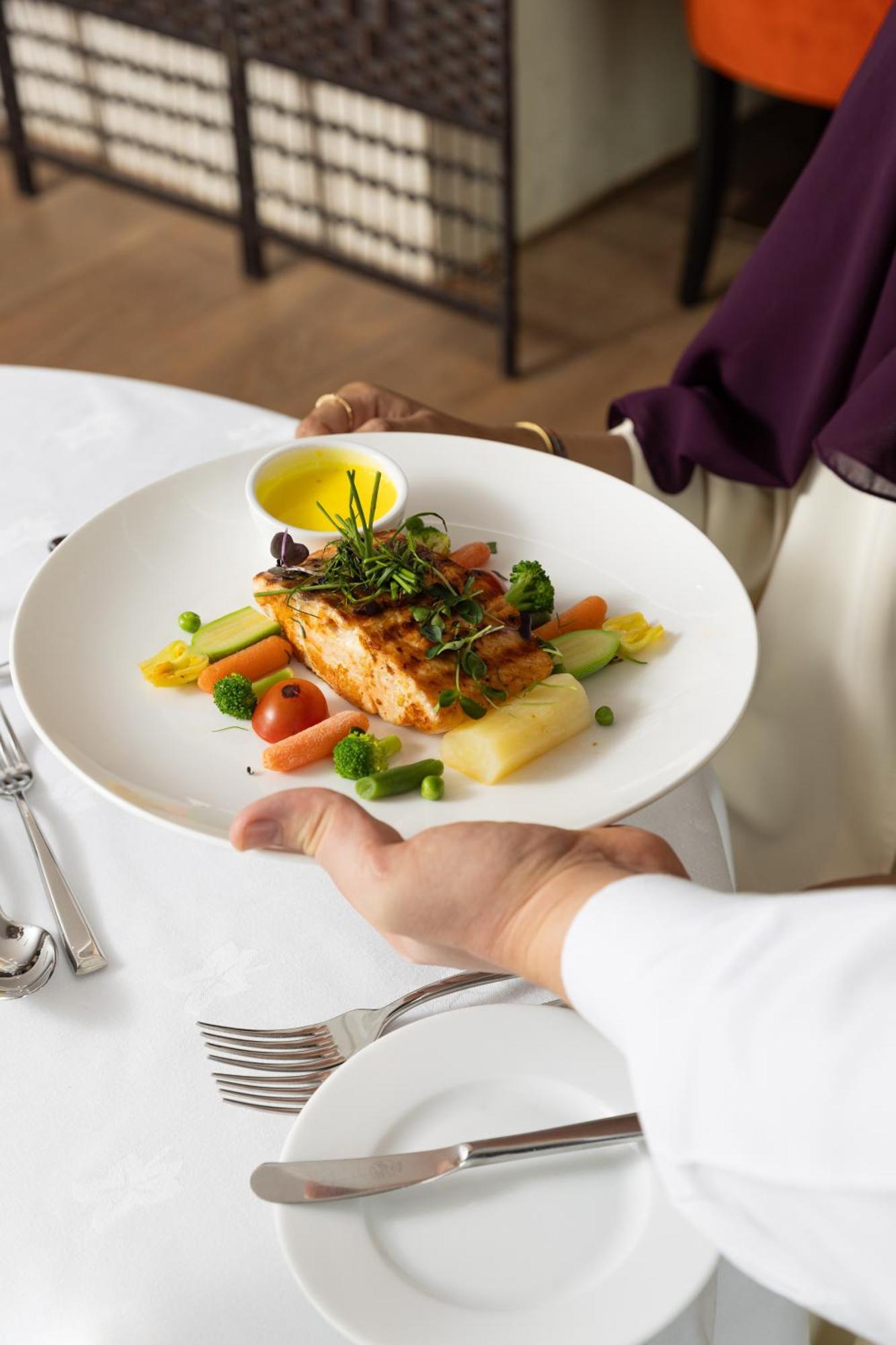 Sofitel Shahd Al Madinah Hotel Medina Exterior photo The photo shows a plate of food being presented. The dish features a piece of grilled salmon on a bed of vegetables, including small tomatoes, green peas, and other colorful vegetables. There is also a drizzle of yellow sauce, likely a dressing or oi